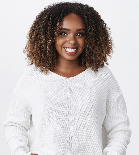 A black woman wearing a white sweater and jeans smiling.